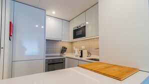 Uma cozinha moderna com armários brancos, micro-ondas, cafeteira e tábua de corte de madeira no balcão.
