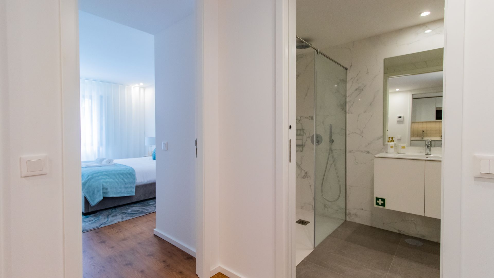 Une chambre d’hôtel avec une douche en verre, un lit recouvert d’une couverture bleue et une salle de bain avec un mur de douche en marbre et un grand miroir.