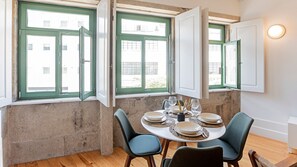A dining area with a round table set for four, two chairs on each side, and a view of a building through green-framed windows.