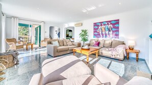 Un salon spacieux avec un grand canapé, une table basse et un coin repas. Une grande fenêtre laisse entrer la lumière naturelle et offre une vue sur l’extérieur.