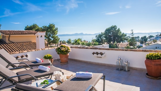 Une terrasse sur le toit, aménagée avec des chaises longues, des plantes en pot et offrant une vue sur la mer et les montagnes lointaines.