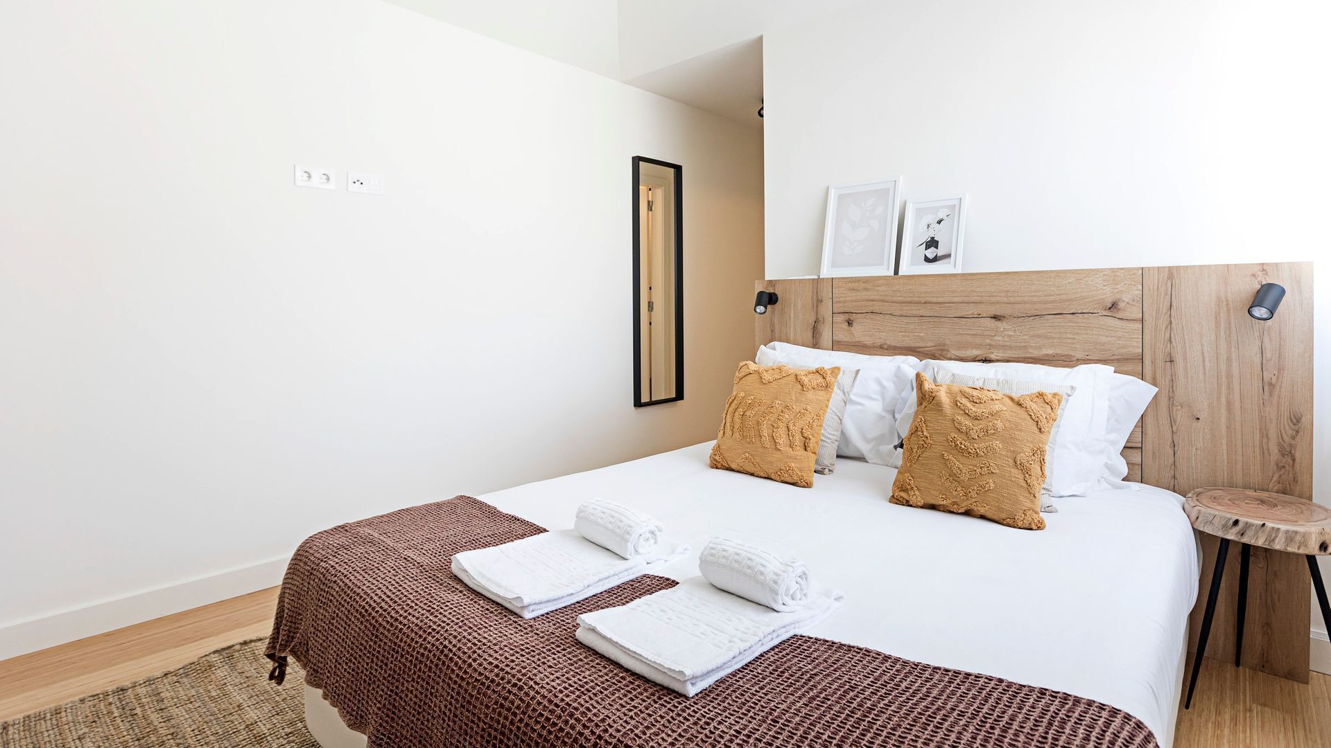 A hotel room with a wooden headboard, white bedding, and a brown woven throw blanket.
