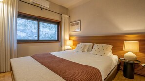 Une chambre d’hôtel avec un grand lit, deux lampes de chevet, une fenêtre avec des rideaux et un climatiseur fixé au mur.