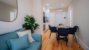A modern living room with a blue sofa, a dining table set for four, and a kitchen in the background. - Almada 1.3 by LovelyStay (Porto)