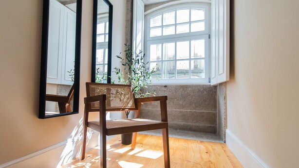 A corner room with a wooden chair, a large mirror, and a window with a view of a building. - Almada 1.3 by LovelyStay (Porto)
