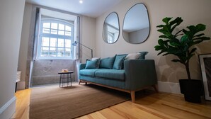 A modern living room with a teal sofa, a large mirror, a potted plant, and a view of the outside through a window. - Almada 1.3 by LovelyStay (Porto)