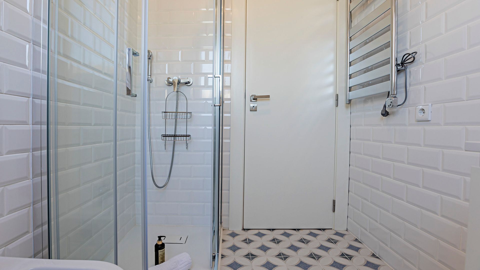 Une salle de bain moderne avec une douche à parois de verre, un espace de douche carrelé de carreaux blancs et un sol à motifs.