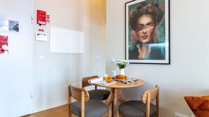 A modern room with a round wooden table, two chairs, a painting on the wall, and a whiteboard.