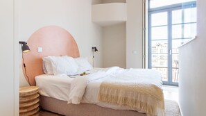 Une chambre à coucher avec un lit, des lampes de chevet, une table ronde en bois et une grande fenêtre donnant sur un beau paysage.