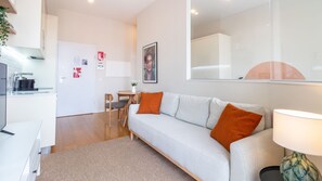 Un appartement moderne doté d’une kitchenette, d’un canapé avec des coussins orange, d’un coin repas et d’un grand miroir.