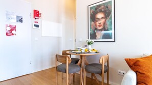 Un petit coin repas avec une table ronde, deux chaises et un tableau accroché au mur.