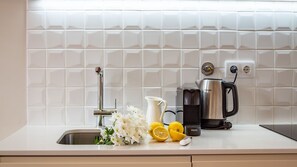 Un plan de travail de cuisine avec un évier, une machine à café, une bouilloire, ainsi que quelques citrons et des fleurs.
