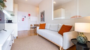 A modern living room with a sofa, a coffee table, and a lamp. There is a kitchen area with a refrigerator and a sink.