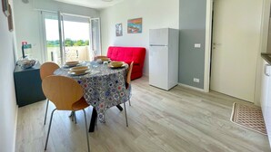 Ett kompakt bostadsutrymme med ett matbord, stolar, en röd soffa, ett kylskåp och en dörr.