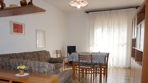 A living room with a patterned sofa, a wooden dining table with chairs, and a tiled floor. - Holiday Home in Caorle Near Spiaggia Tartaruga (Caorle)