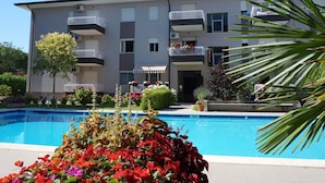 A modern multi-story building with balconies, a swimming pool, and various plants. - Holiday Home in Caorle Near Spiaggia Tartaruga (Caorle)