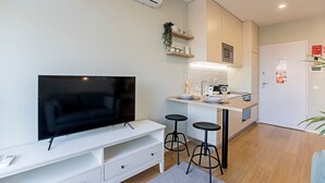 Una cocina moderna con microondas integrado, una pequeña isla con taburetes y un televisor de pantalla plana sobre un mueble blanco.