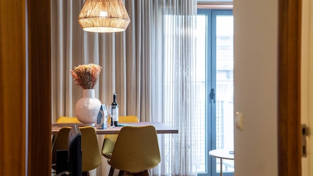 A dining area with a table, chairs, a vase with dried flowers, a wine bottle, and a hanging light fixture. - Firmeza388 1E - Charming Apartment by LovelyStay (Porto)