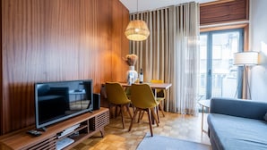 A modern hotel room with a wooden wall, a flat-screen TV, a dining table with chairs, a sofa, and a floor lamp. - Firmeza388 1E - Charming Apartment by LovelyStay (Porto)