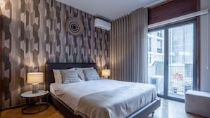A modern hotel room with a geometric-patterned wall, a large bed with a grey blanket, two bedside lamps, and a view of the outside balcony. - Firmeza388 1E - Charming Apartment by LovelyStay (Porto)