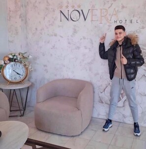 A modern hotel interior with a round armchair, a decorative clock, and a sign for 'NOVERA HOTEL'. - Hotel Novera (Timisoara)
