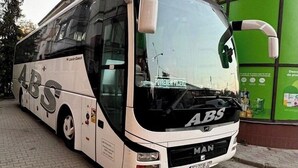 A white and black MAN bus with the logo "ABS" on its side, parked in front of a building with a green advertisement board. - Hotel Novera (Timisoara)