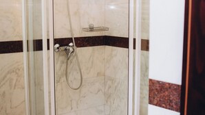 A glass-enclosed shower stall with a handheld showerhead and a wall-mounted faucet. - Hotel Novera (Timisoara)