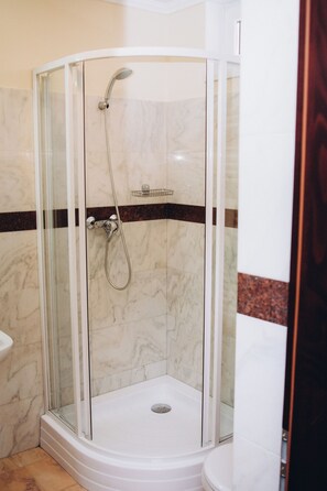 Cabina de ducha con paredes de vidrio, cabezal de ducha de mano y grifo empotrado.