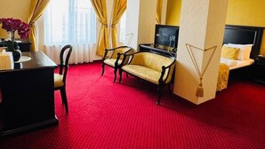 A hotel room with a red carpet, a sofa, a TV, a bed, and a desk with a lamp. - Hotel Novera (Timisoara)