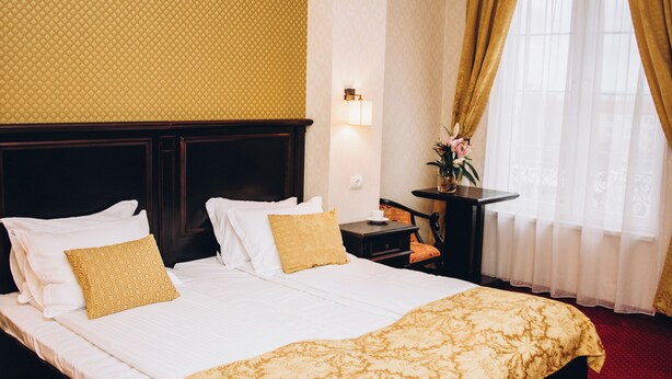 A hotel room with a large bed, a nightstand, a desk, and a window with curtains. - Hotel Novera (Timisoara)