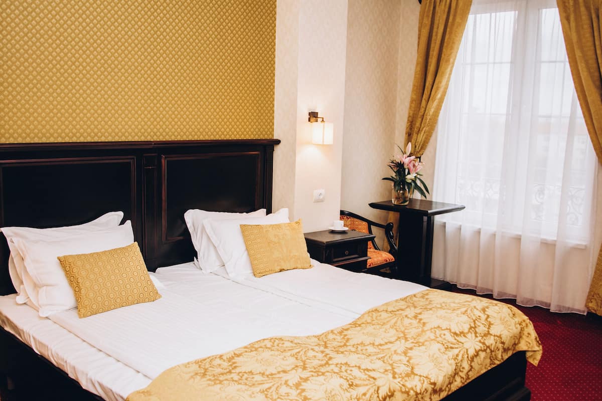 Quarto de hotel com uma cama grande, mesa de cabeceira, escrivaninha e janela com cortinas.
