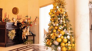 A Christmas tree decorated with gold and silver ornaments in a warmly lit room with a fireplace and a clock on the wall. - Hotel Novera (Timisoara)
