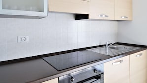 A modern kitchen with light wood cabinets, a black countertop, a stainless steel sink, and a built-in oven. - Apartment at Lago di Como Near Dervio Beach (Dervio)