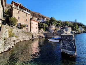 A stone building with a balcony, a clear waterfront, and a small boat docked. - Apartment at Lago di Como Near Dervio Beach (Dervio)