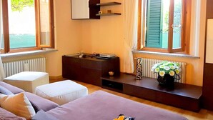A bedroom with a bed, a dresser, a vanity, and a window with curtains. - Belvilla by OYO Casa Cristina Meina Centro 4 (Meina)
