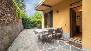 A stone-floored patio with a table and chairs, a balcony, and a door leading inside. - Belvilla by OYO Casa Cristina Meina Centro 4 (Meina)