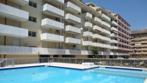 Ein Schwimmbecken mit einer gefliesten Terrasse, umgeben von einem weißen Zaun.