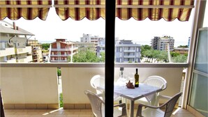 Ein Balkon mit Tisch und Stühlen, einer Weinflasche und Blick auf Stadt und Meer.