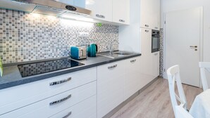 A modern kitchen with white cabinets, a black countertop, a tiled backsplash, a toaster, a kettle, and a built-in oven.