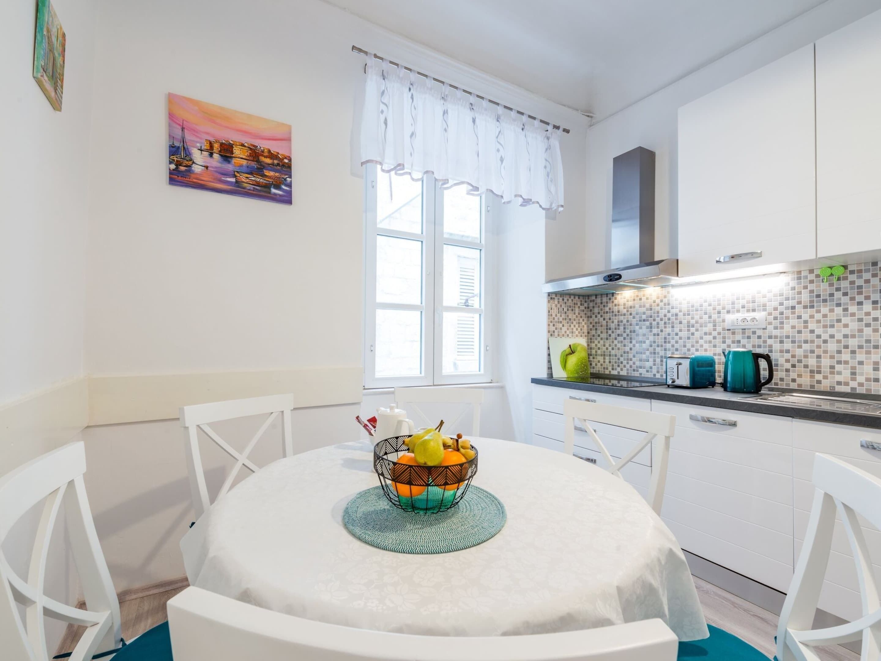 Una cocina moderna con gabinetes blancos, un salpicadero de azulejos y un ventanal con cortinas blancas.