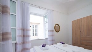 A bedroom with two beds, a wooden wardrobe, a window with curtains, and a mirror on the wall.