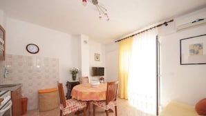A compact kitchen with a dining table and chairs, a clock, and a window with curtains. - Apartments Mira - One Bedroom Apartment With Balcony (Supetar)