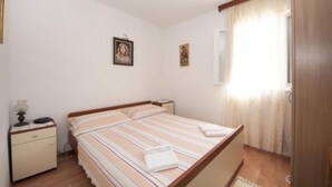 A bedroom with a double bed, bedside tables, a nightstand, and a window with curtains. - Apartments Mira - One Bedroom Apartment With Balcony (Supetar)