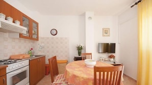A compact kitchen with wooden cabinets, a stove, and a dining area with a table and chairs. - Apartments Mira - One Bedroom Apartment With Balcony (Supetar)