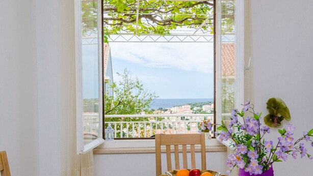 Un balcon avec une table, une chaise, un panier de fruits et un vase de fleurs.