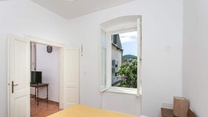A bedroom with a bed, a window, a door, and a small table with a lamp. - Apartment Tranquilo- Two Bedroom Apartment With Garden View (Dubrovnik)