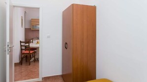 A room with a wooden wardrobe, a dining table with chairs, and a kitchen area visible through an open door. - Apartment Tranquilo- Two Bedroom Apartment With Garden View (Dubrovnik)