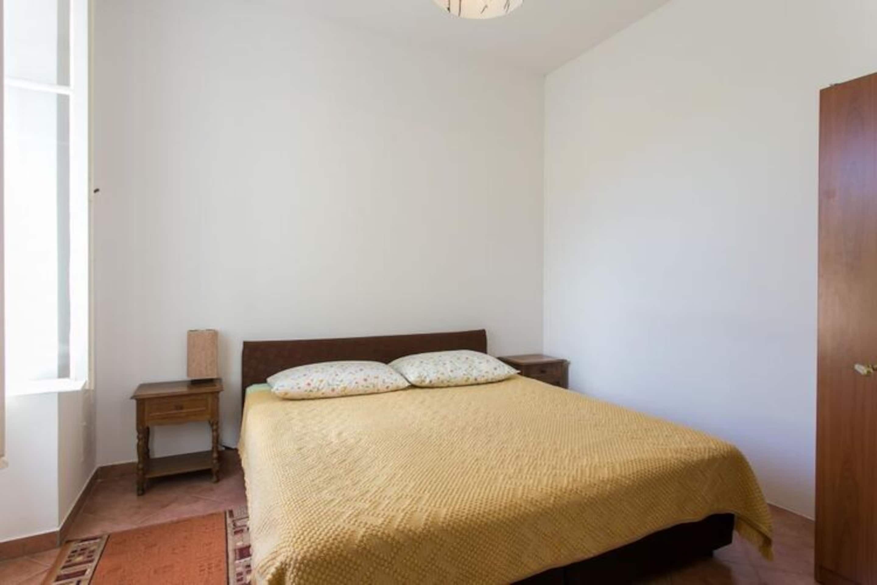 Ein Schlafzimmer mit einem Bett, einem Nachttisch, einer Holztür und einem Fenster.