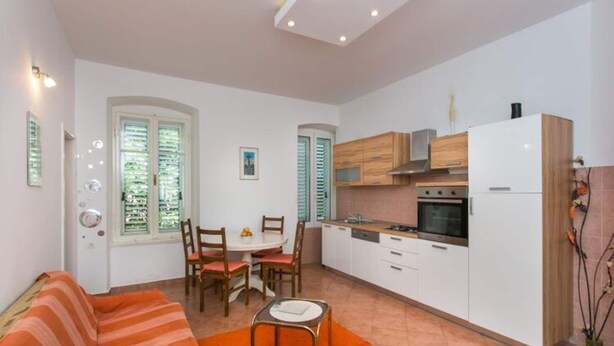 A compact living space with a kitchenette, a dining area, and a sofa. - Apartment Tranquilo- Two Bedroom Apartment With Garden View (Dubrovnik)