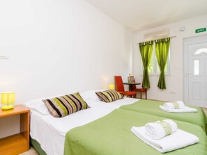A hotel room with a bed, a desk with a chair, a table with a chair, a window with curtains, and an exit sign.